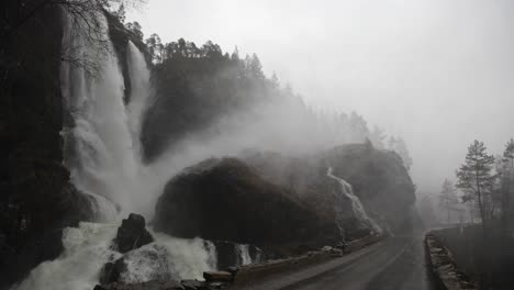 close view of bridge and road wet from mist and flooding near hesjedalsfossen. waterfall overflows during heavy rainstorm in western norway