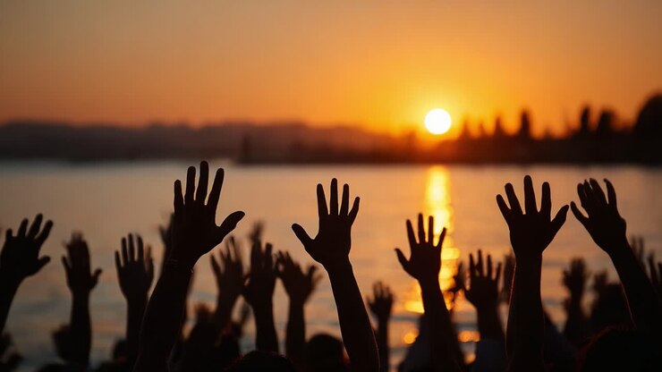 Celebrating Togetherness: A Group of Hands Raised in Unison Against a Glorious Sunset, Symbolizing Unity, Hope, and Shared Aspirations by the Tranquil Waterside