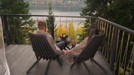 a couple in love sitting on a balcony overlooking a lake with a view of the forest and mountains