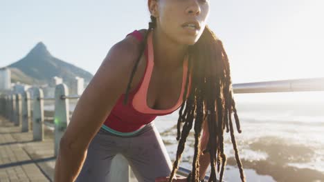 mujer afroamericana haciendo ejercicio descansando en el paseo marítimo junto al mar