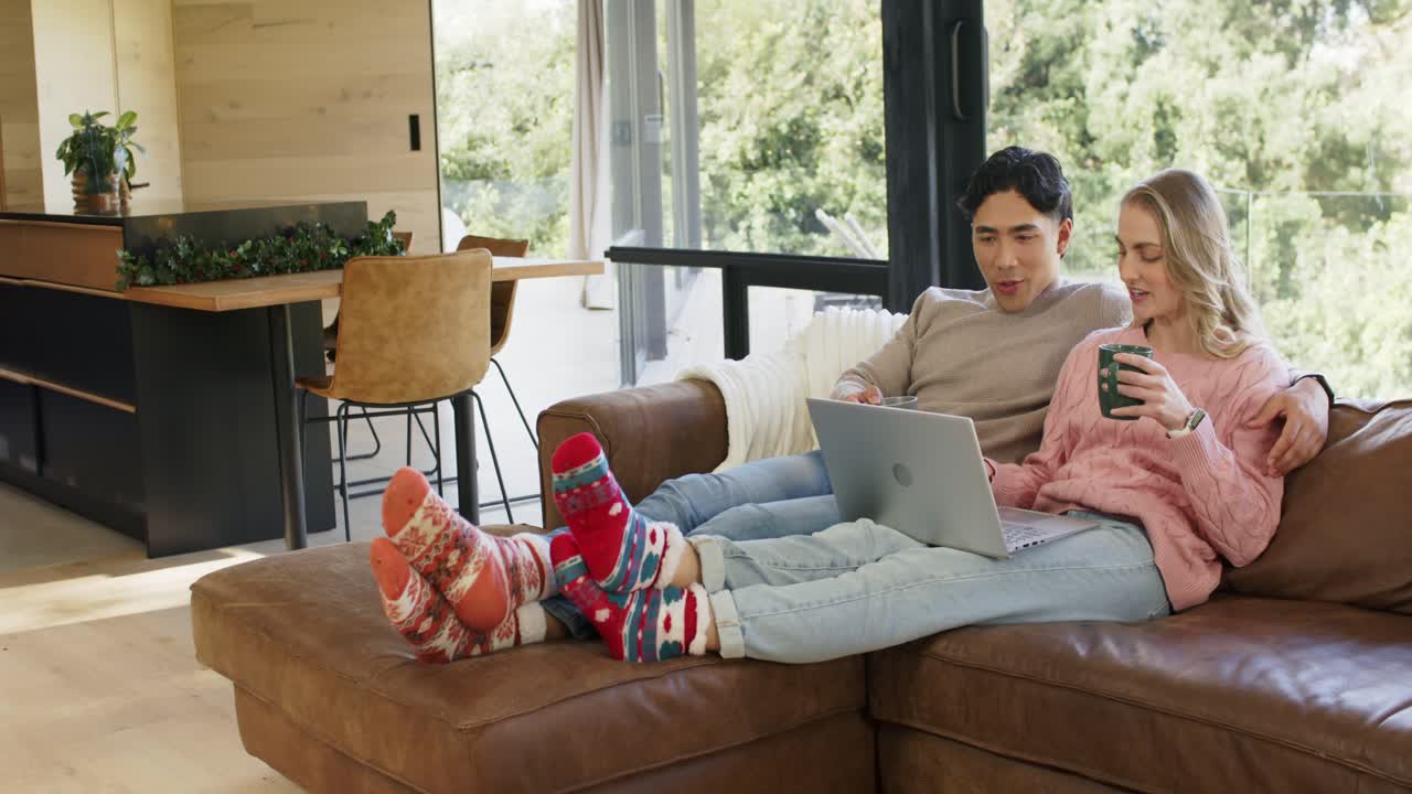 Couple opening laptop and discussing content while sipping coffee and typing on brown leather couch