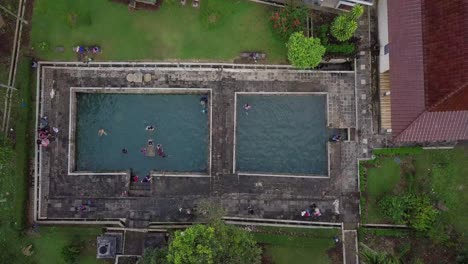 Ascending-top-down-shot-of-people-in-swimming-pool-having-fun-at-Famous-Umbul-Temple,Central-Java-during-cloudy-day