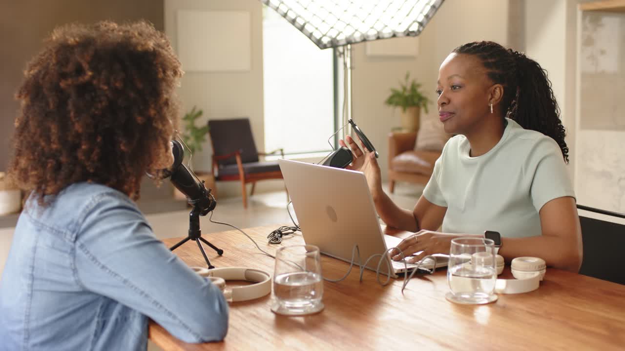 Diverse co-conduttrici sorridenti che digitano su un laptop, registrando un podcast in uno studio domestico, spazio per la copia