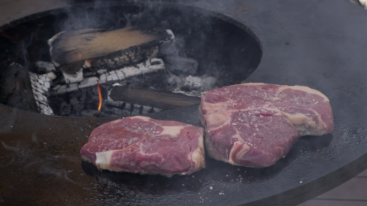 Raw beef steaks sizzling on outdoor plancha grill