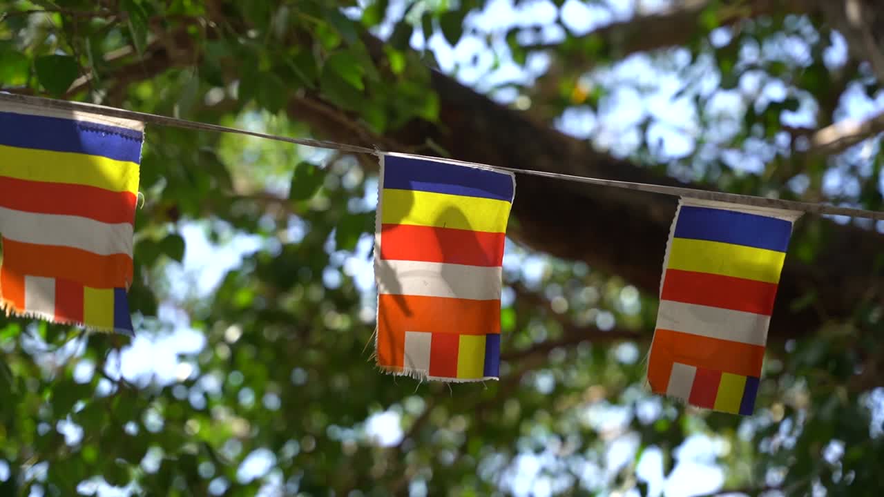Globally used Buddhist flag dating from the 19th century as a universal symbol of Buddism, quietly waves on a flag line in the wind near the Dambulla cave temple in Sri Lanka. Slowmo close up shot