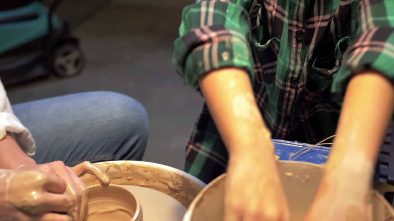 Boy and woman makes a pot with pottery wheel in a workshop
