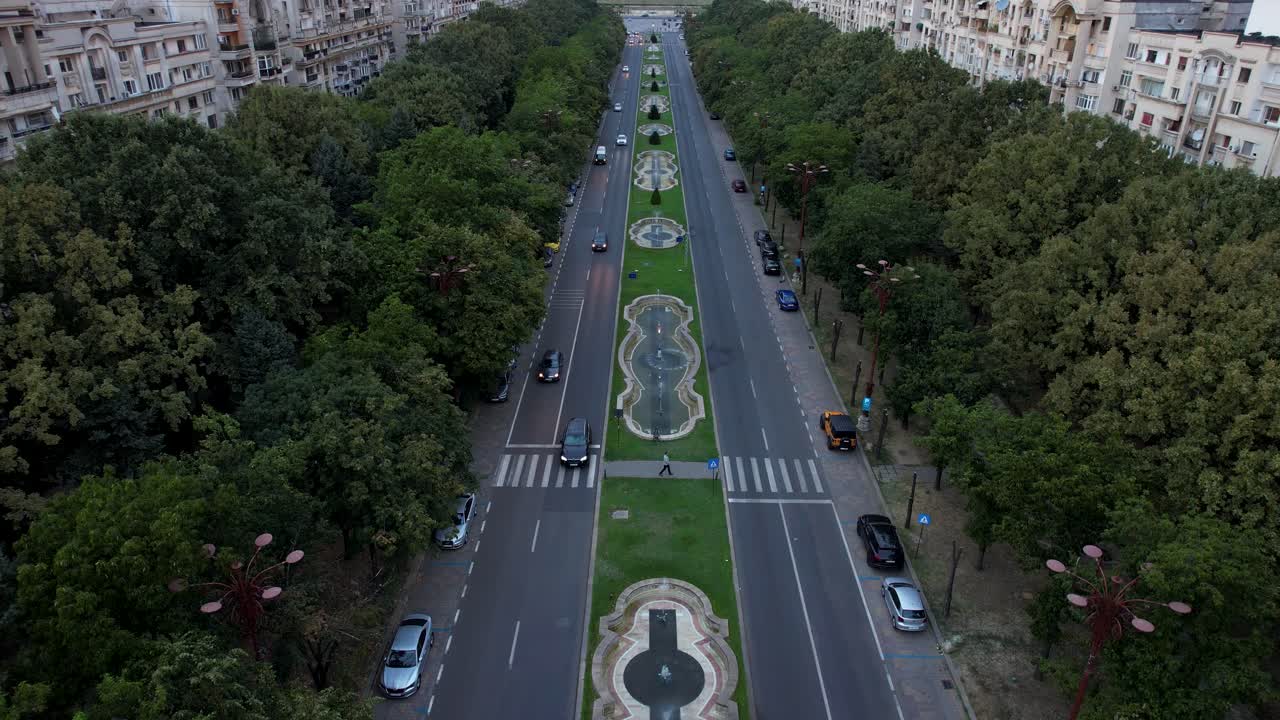 Stunning Slow-Motion Aerial Reveal of the Palace of Parliament in Bucharest, Romania at Sunset, with Orange Sky, Lush Vegetation, and Dancing Water Fountains