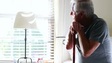 Thoughtful-senior-man-with-his-walking-stick-in-the-bedroom