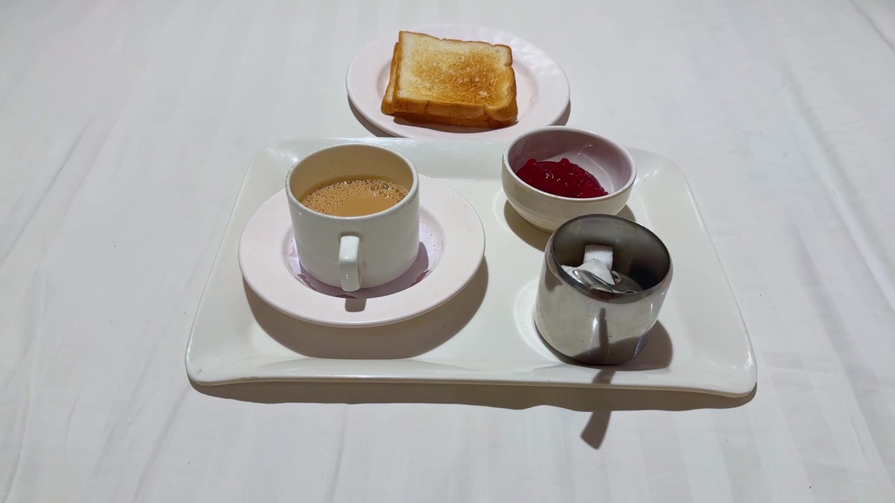 Vidvinkelperspektiv i førsteperson av nyservet indisk melkete med ristet brød, syltetøy og sukkerbiter arrangert på et frokostbrett, klar til å nytes