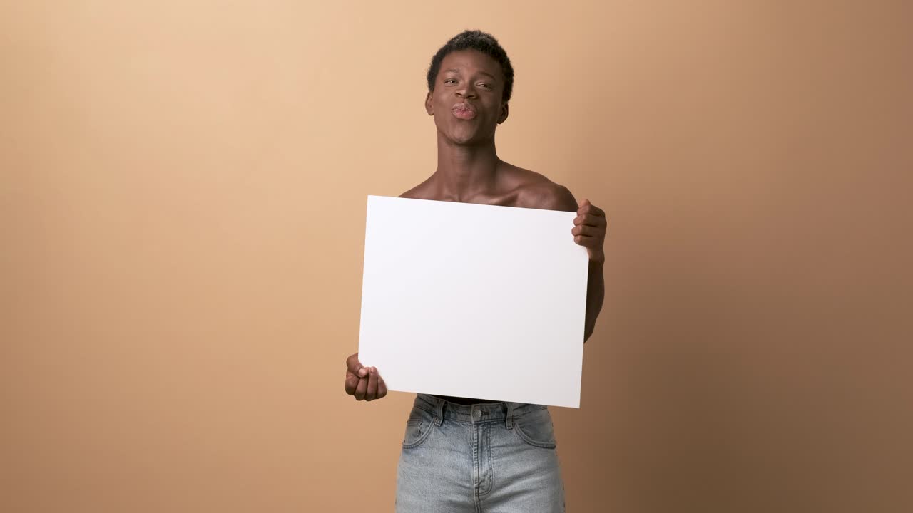 Smiling african black man shirtless holding a blank panel over beige background