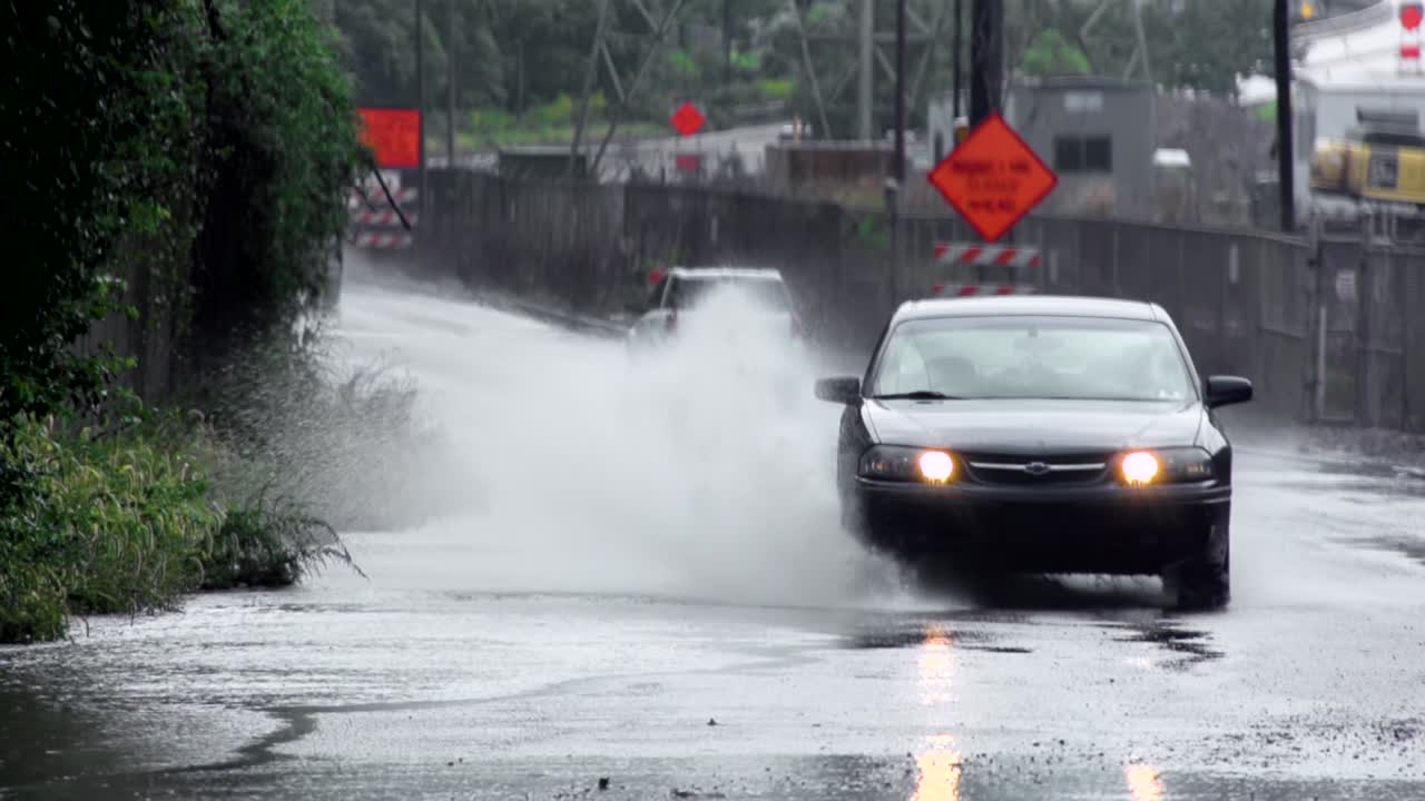 Car driving through large puddle by the US Steel Edgar Thomson Steel Plant in Braddock, Pennsylvania. Raining. Static shot.