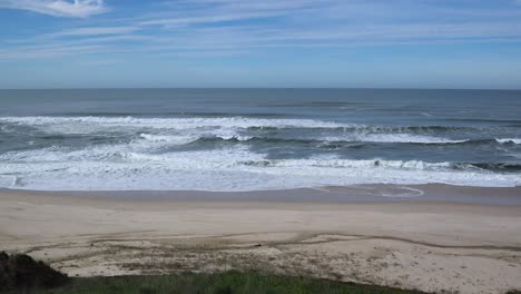 waves crashing on to sandy beach with blue skies and horizon line visible, atlantic ocean, portugal