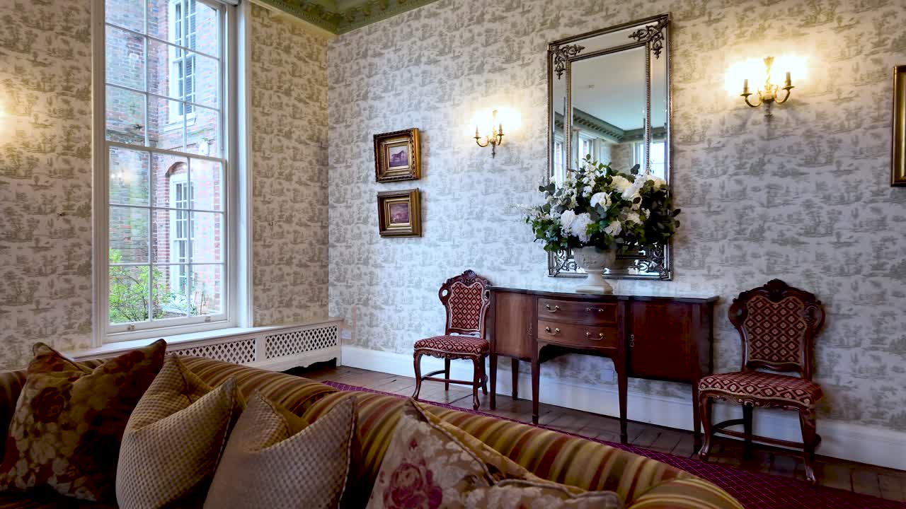 Elegant Manor Home Interior In England With Antique Furniture Floral Wallpaper And Large Window Overlooking Garden Creating A Sense Of History And Sophistication