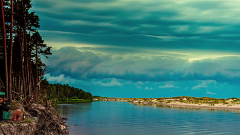 A-young-woman-on-the-shore-of-a-beach-watches-kayaks-in-a-canal---stormy-cloudscape-time-lapse