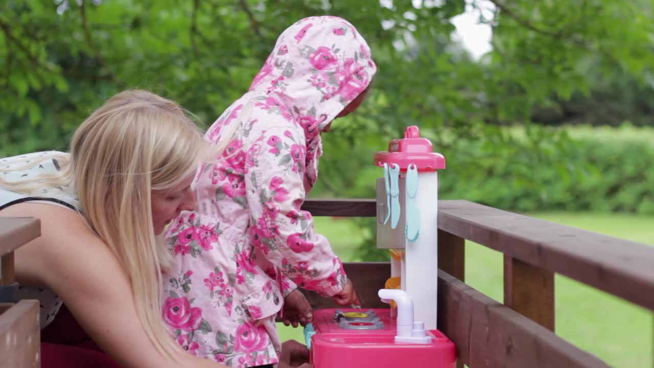 Biracial sweet family moments, European mom playing outdoor with African daughter with plastic kitchen toy, little chef cooking food, exterior garden, static day