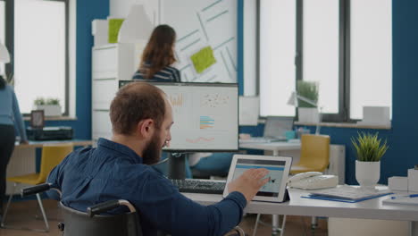 Businessman-with-disabilites-using-computer-and-tablet-comparing-graphs