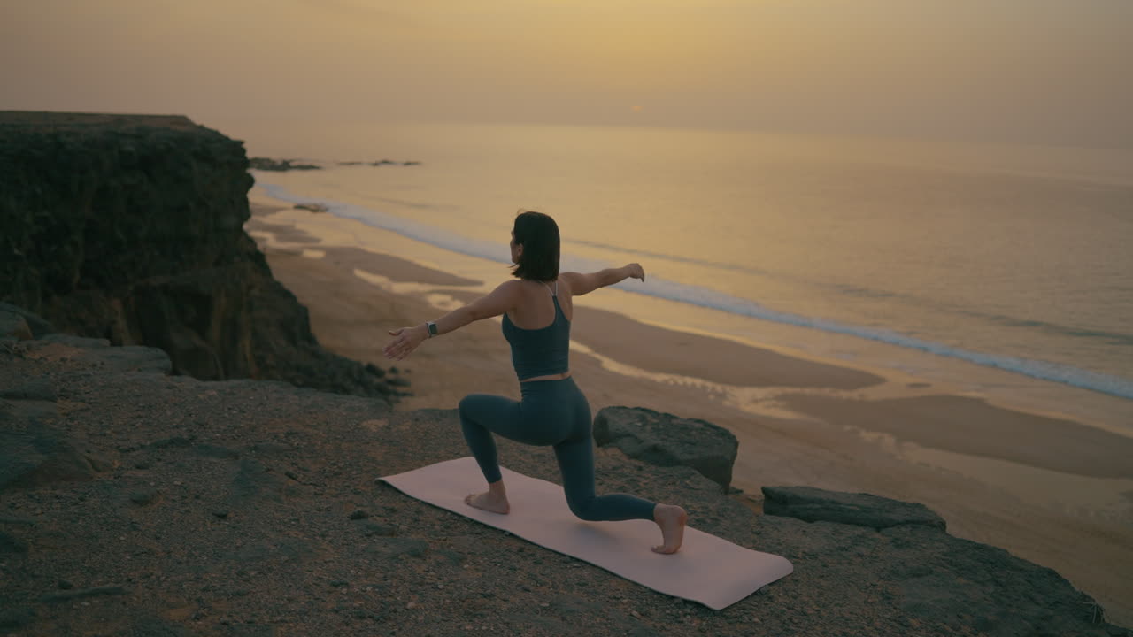 Donna che pratica yoga all'alba o al tramonto su una scogliera a picco sulla spiaggia