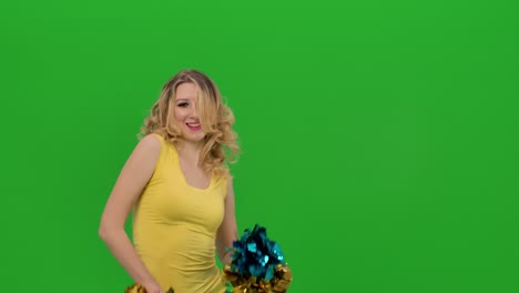 una animadora mueve vigorosamente sus caderas, brazos pom-pom, giros y ondas de su cabello. una chica con un uniforme amarillo-azul está bailando un baile jubiloso en el estudio en una pantalla verde. cerca. cámara lenta