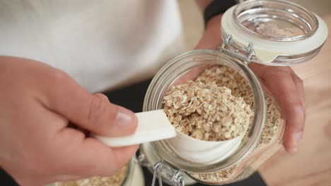 person scoops spoonful of oat flakes from jar, slow motion close up