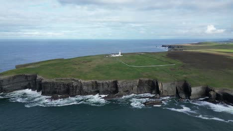 loophead lighthouse on rugged cliffs with waves crashing, cloudy sky, aerial view