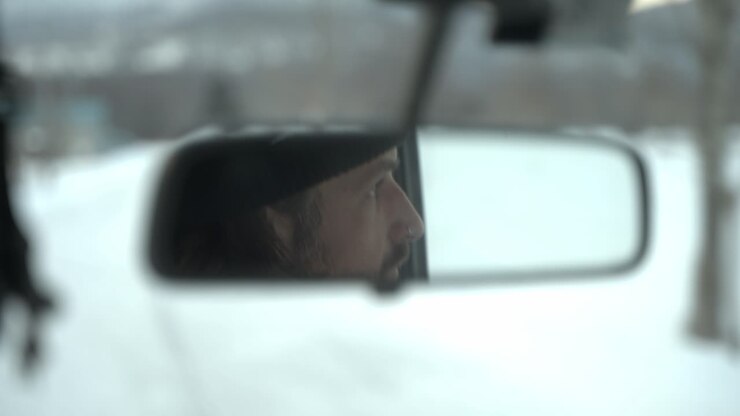 Man drives through snowy Hokkaido seen in rearview mirror with focus on his thoughtful expression