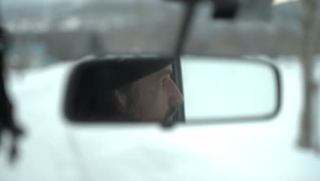 man drives through snowy hokkaido seen in rearview mirror with focus on his thoughtful expression