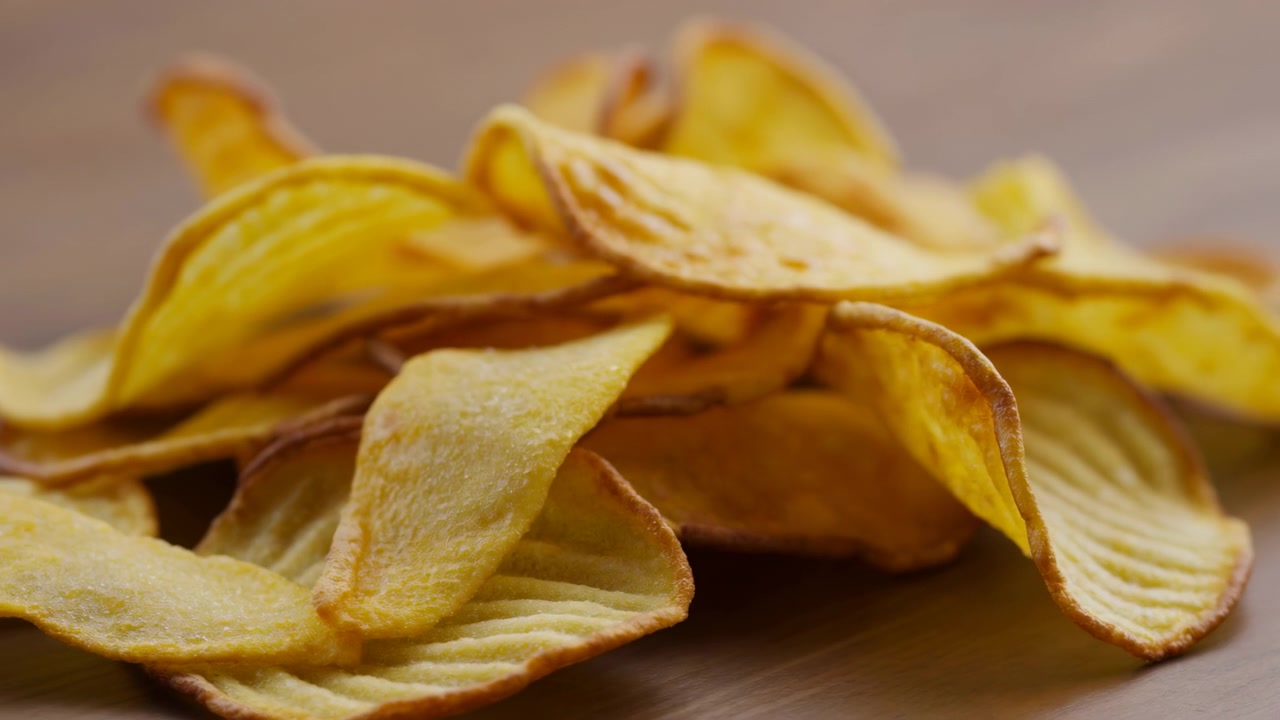 Close-up of stacked potato chips displayed on a neutral background, captured from a top-down perspective. The chips are neatly arranged, showcasing their vibrant yellow and brown colors.
