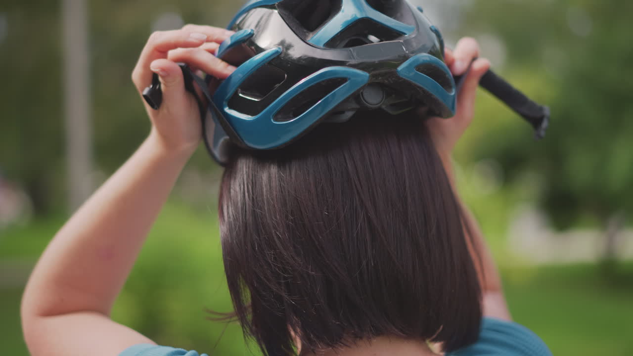 woman adjusting bike helmet in park, removing sunglasses and checking strap, short bob haircut, calm focus before urban commute, soft sunlight and green trees along pathway, safety routine