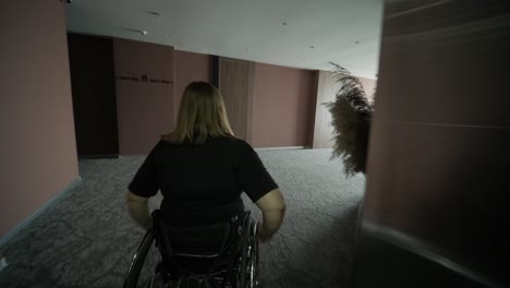 una mujer en silla de ruedas está dentro de un ascensor, sosteniendo un artículo en sus manos, mientras espera que el ascensor llegue a su piso. la imagen destaca la accesibilidad, la independencia y la infraestructura moderna.