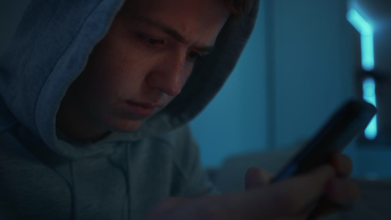 enfoque adolescente caucásico usando teléfono móvil mientras está sentado por la noche en su habitación.