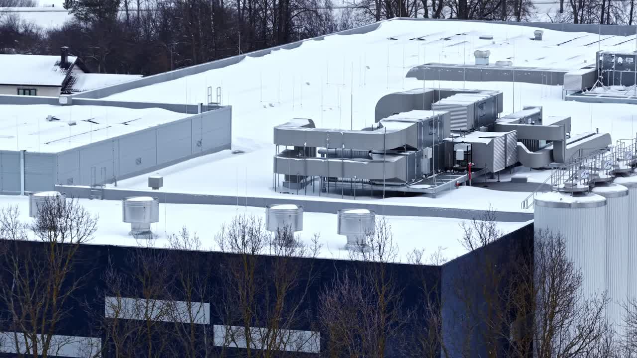 Aerial winter view of a factory rooftop with HVAC ventilation equipment and tall storage silos, covered in snow at an industrial site