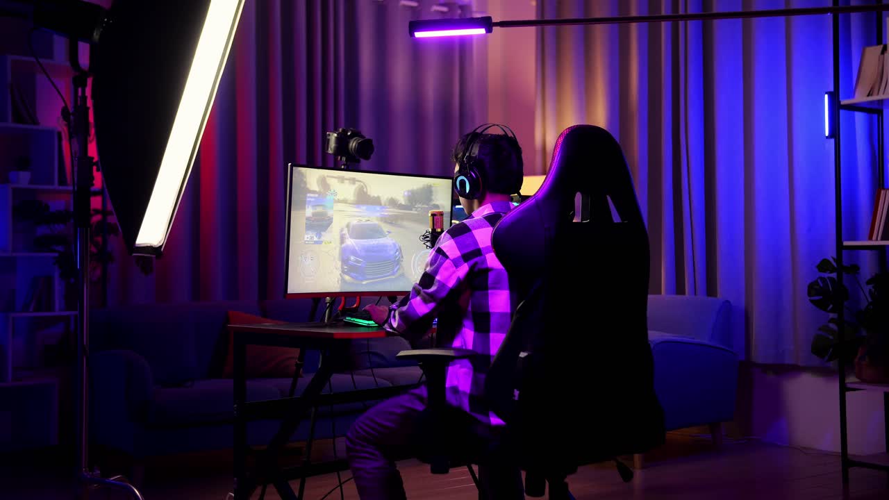 vista trasera de un chico asiático que juega a un juego de carreras de coches a través de la red en una computadora personal. desafío y competidor de intimidación, videojuego de transmisión en vivo, escritorio iluminado por luz de tira led rgb