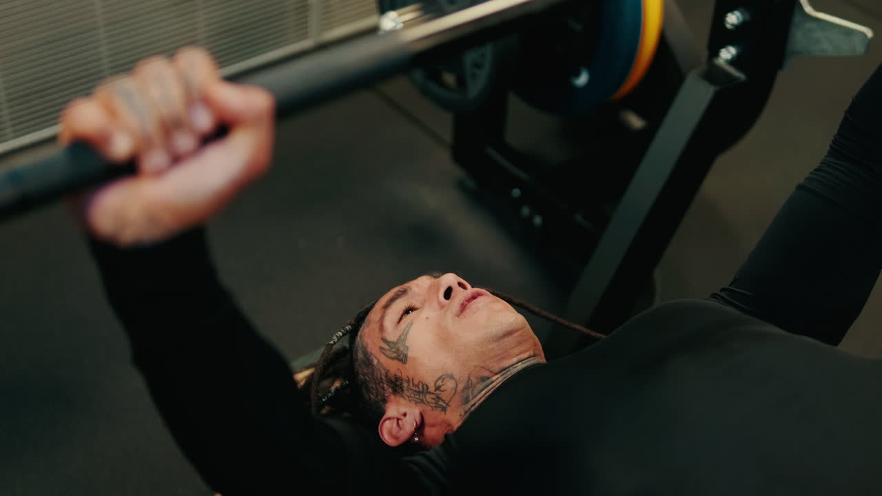 Pria Bertato dengan Rambut Gimbal Melakukan Bench Press di Gym