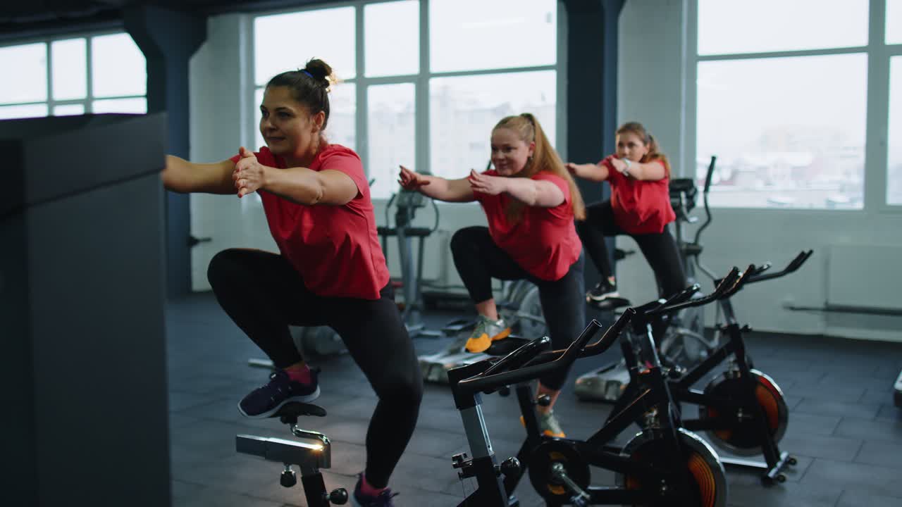 Group of smiling friends women class exercising training spinning on stationary bike at modern gym