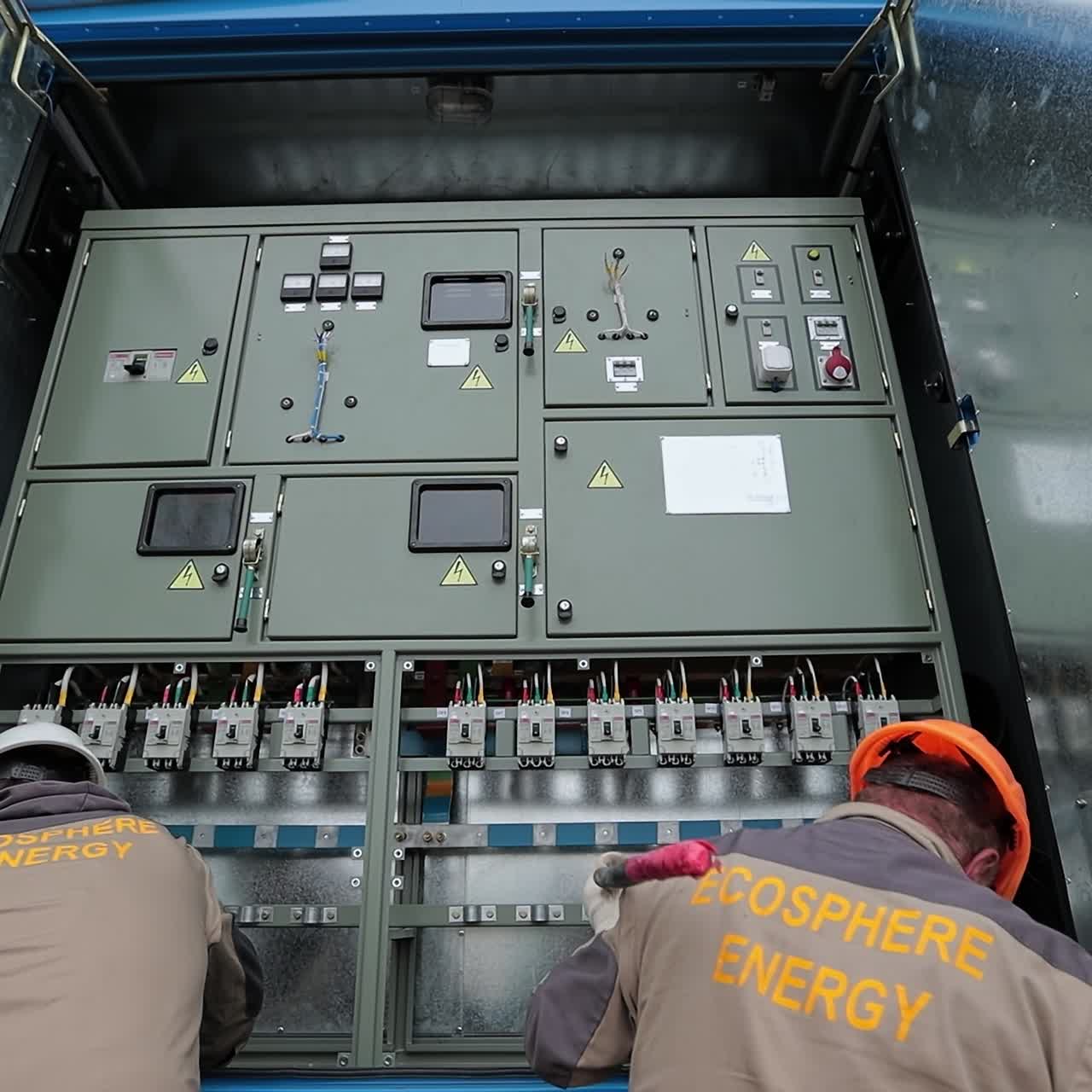 Engineers standing in front of the equipment in a hanging metal booth. Men trying to adjust thick cables to the equipment in the booth