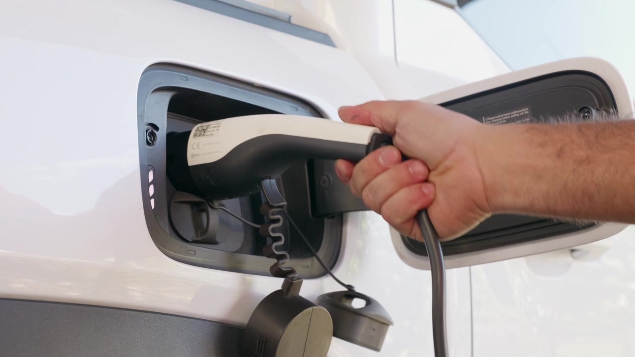 Bir kişinin elektrikli aracı şarj cihazına takmasının yakın çekimi. Elektrikli araç şarjı, temiz ulaşım, yenilenebilir enerji, sürdürülebilirlik ve mobilite geleceğini temsil eden konsept görüntüler.