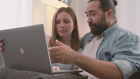 una pareja feliz tiene una conversación relajada sentada en el sofá y mirando la computadora portátil 1