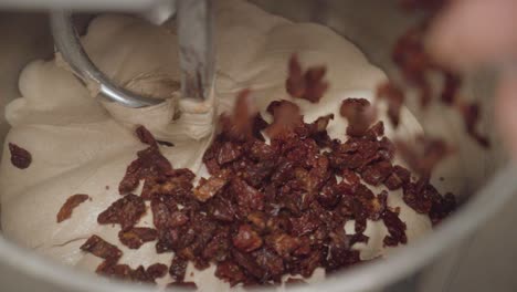 adding dried tomatoes into the dough in electric mixer for bread preparation