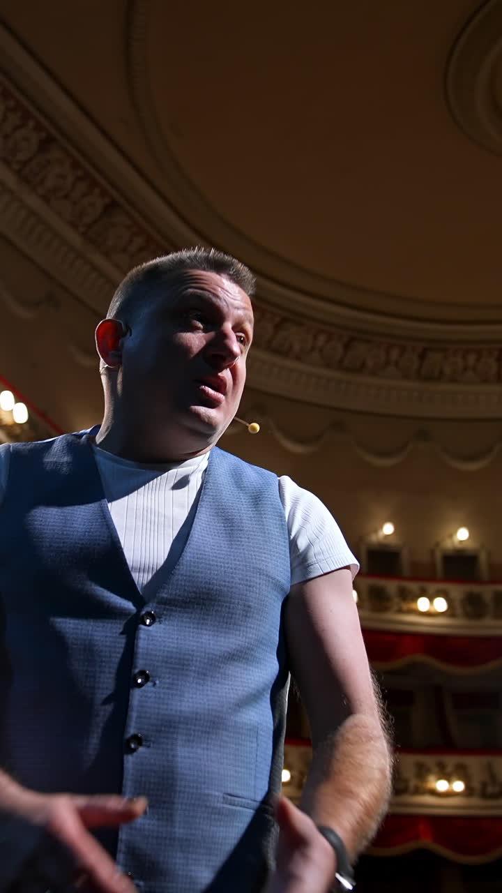 Man on stage gesticulating and talk. Professional actor performing his role on spotlight background in theater. View from stage. Vertical video