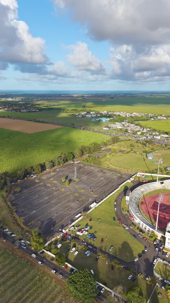 Vertical aerial view over the Stade Anjalay in Mauritius, highlighting the huge car park covered in tire marks from a high-speed racing or drifting event next to the main stadium