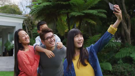 Feliz-Hija-Asiática-Tomando-Selfie-Con-Feliz-Madre-Y-Padre-Llevando-A-Cuestas-A-Su-Hermano,-En-El-Jardín