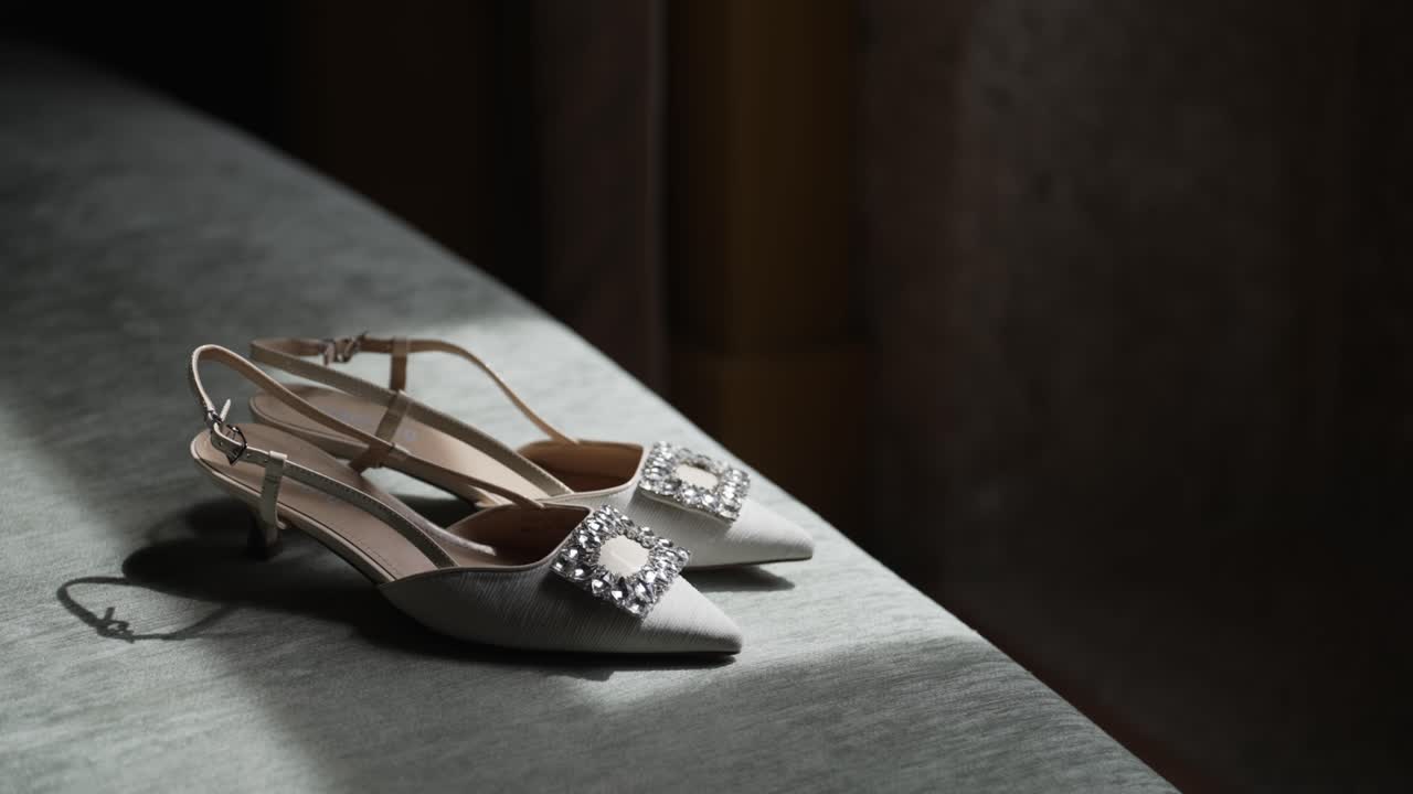 Elegant white bridal heels with jeweled buckles placed on soft fabric in gentle light
