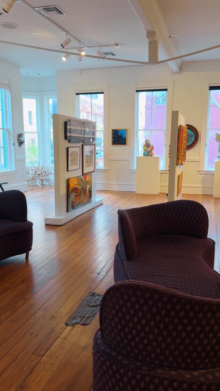 Orlando, USA, 5 giugno 2025: Interno di una galleria d'arte moderna con dipinti e divani viola. Luminosa sala espositiva con opere d'arte contemporanea su pareti bianche e sedute curve viola.