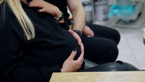 cropped image of a blonde woman wearing a hoodie and being pregnant at the last stages. male hand pets her big belly.