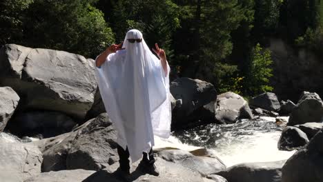 dressed up as a ghost holding up a peace sign next to a flowing river