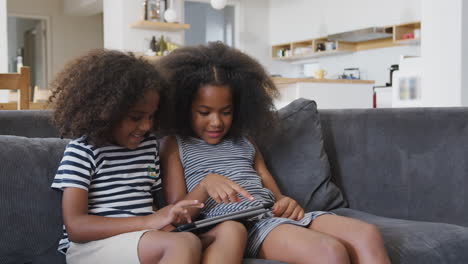 brother and sister sitting on sofa at home playing with digital tablet