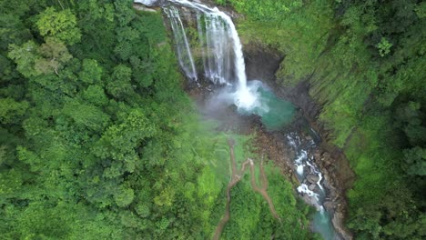 aerial rising of eco chontales waterfall falling into rocky natural pond surrounded by dense green rain forest, costa rica