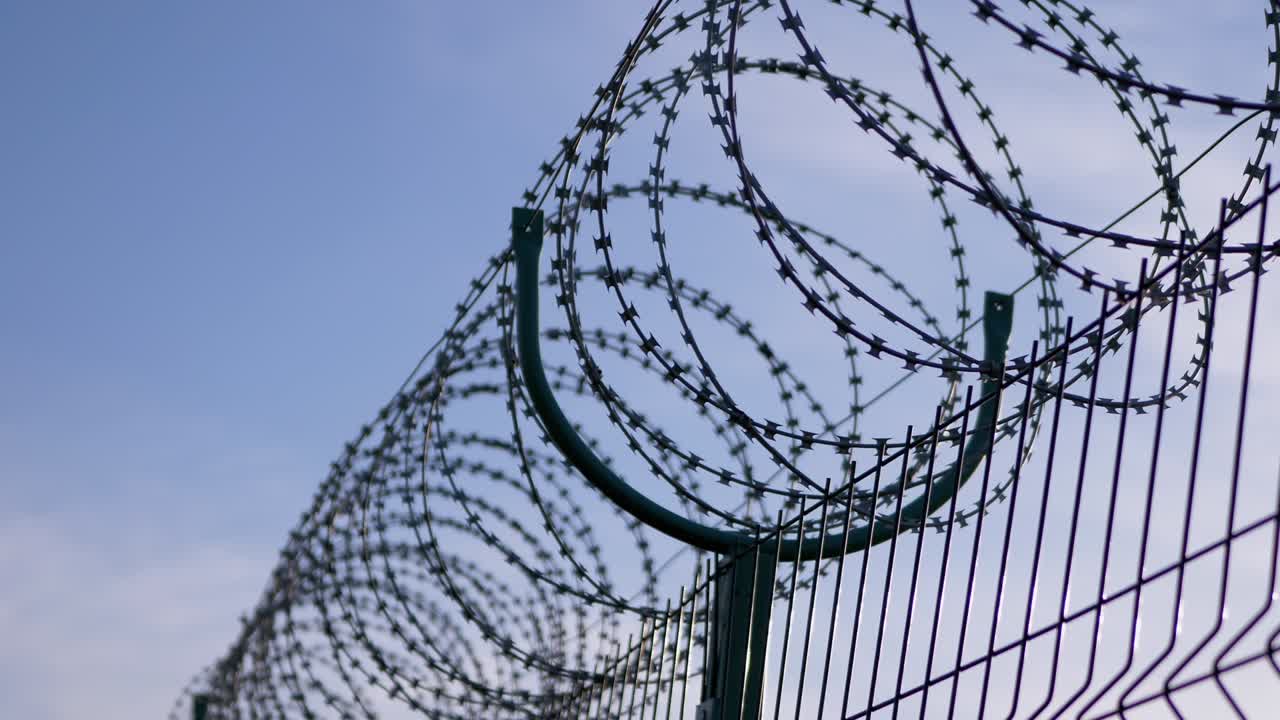 alambre de púas colgado en la frontera de la valla de hierro en contra del cielo azul. 4k