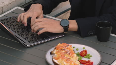primer plano de un hombre de negocios irreconocible que trabaja en una computadora portátil en una cafetería a la hora del almuerzo