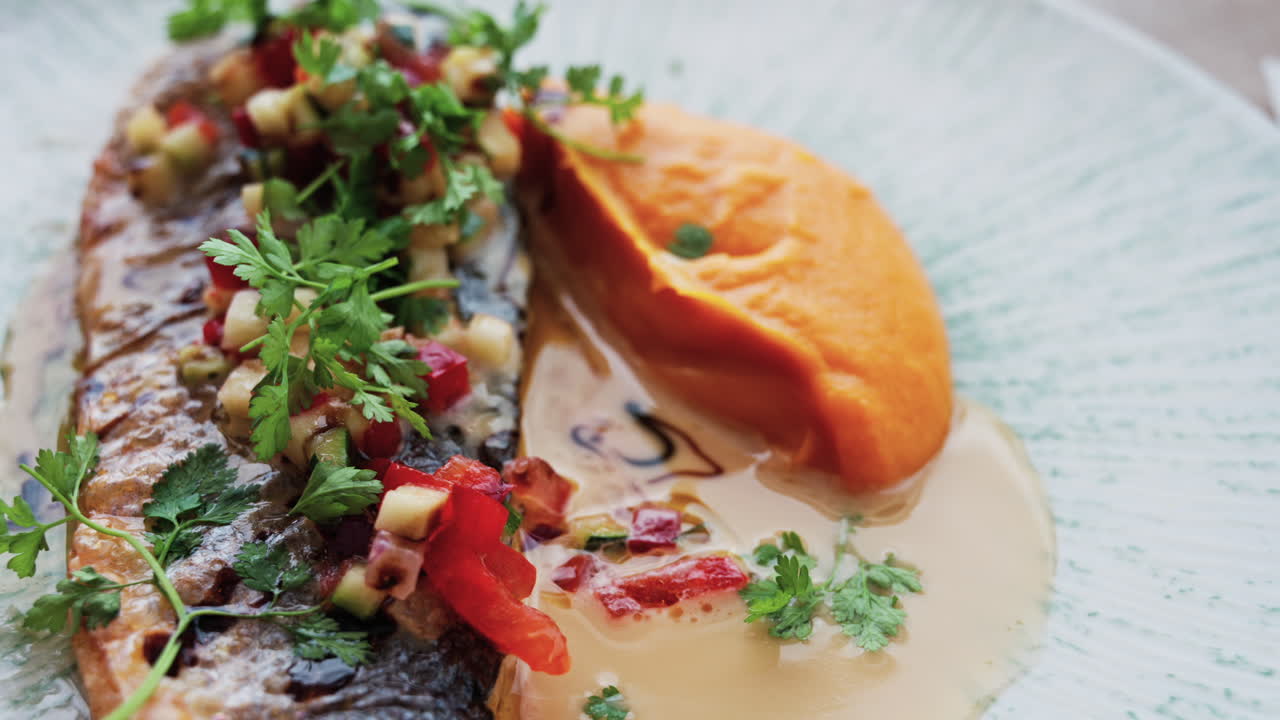 Close up of grilled fish with a sweet potato puree and a sauce on a white plate on a table at a restaurant